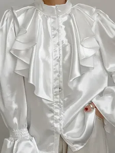 Detailed shot of an elegant white satin blouse with layered ruffles and pearl buttons