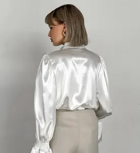 Detailed view of white satin blouse showing glossy fabric and elegant puff sleeves.