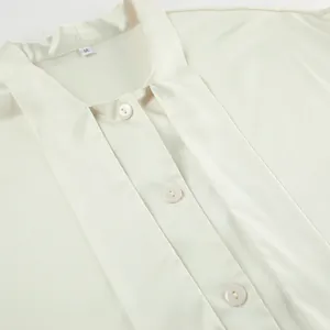 Detailed macro view of cream satin blouse featuring neck tie and pearlescent buttons