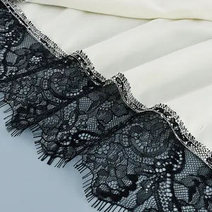 Detailed close-up of elegant black eyelash lace trim on white satin camisole hem