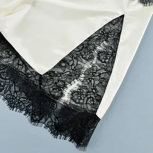Detailed view of the delicate black lace trim on a white satin camisole top