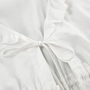 Close-up detail of white cotton-linen blouse showing ruffles and bow tie closure.