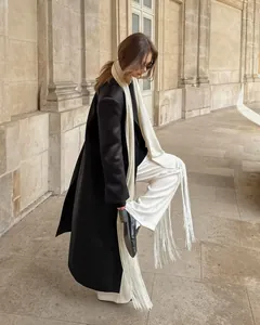 Detail of white satin fringe sash belt styled with a black coat in an elegant setting
