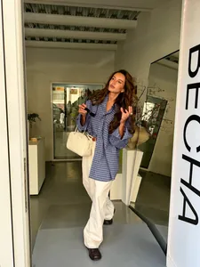 Woman wearing a vintage blue plaid cotton shirt with white trousers in a city setting.