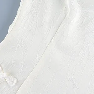 Detail close-up of white jacquard floral fabric and traditional button on blouse.