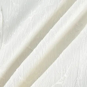 Detail view of white textured fabric with elegant embroidered floral patterns for a shirt.