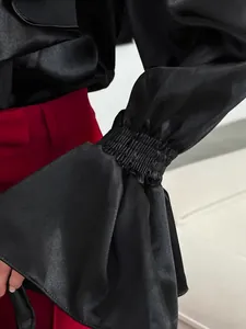 Close-up of elegant black satin flared cuffs with smocked elastic and ruffled hem.