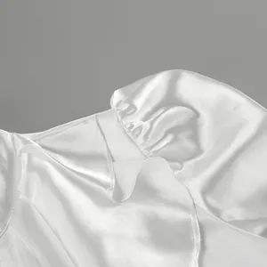 Close-up of white satin blouse showing ruffle detail and glossy fabric texture.