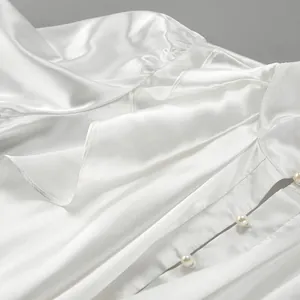 Close-up of white lustrous satin shirt with elegant ruffles and pearl buttons.
