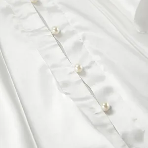 Close-up detail of white satin blouse featuring elegant pearl buttons on smooth fabric