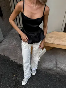 Detailed view of an elegant black satin peplum camisole paired with chic white trousers.