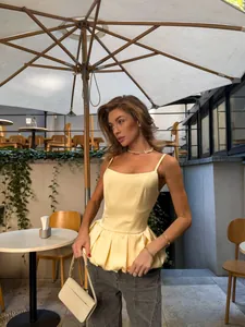 Elegant light yellow peplum camisole vest worn by a model in an outdoor cafe setting