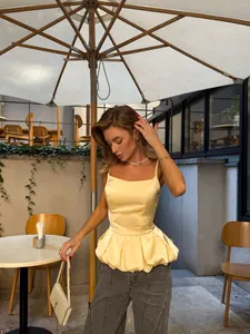 Elegant detail of a yellow satin peplum camisole top worn by a model in an outdoor cafe setting.