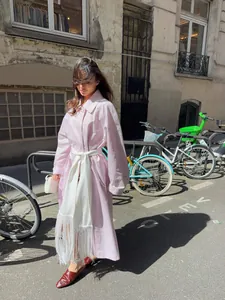 Close-up detail of a pink satin wrap trench coat with a long white fringe tassel belt