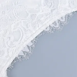 Detailed macro shot of intricate white floral lace with delicate eyelash trim edges.