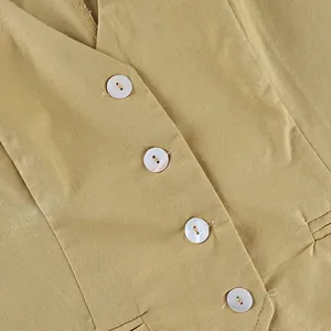 Close-up macro view of delicate white shell buttons on a yellow cotton linen vest garment