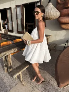 White V-neck camisole holiday dress with straw clutch in an outdoor cafe setting.
