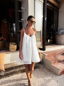 Model wearing a white loose V-neck camisole resort dress on sunlit stone steps