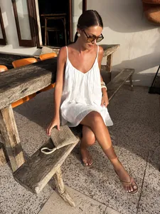 Elegant white V-neck camisole vacation dress worn by a model in a sunlit outdoor patio