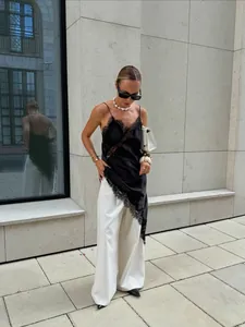 Vue de style rue d'une robe caraco en satin noir avec dentelle et fente latérale.