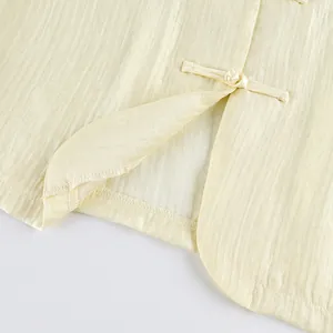 Detailaufnahme traditioneller chinesischer Froschknöpfe an einer hellgelben Retro-Weste