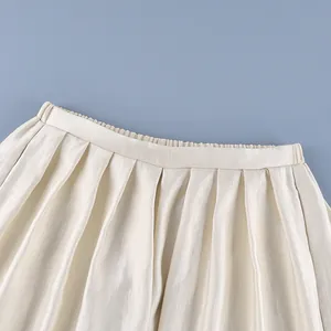 Detailed macro view of cream satin pleated lantern pants featuring elegant texture and waistband
