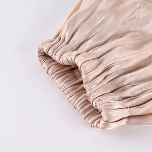 Macro view showing the fine pleated texture and elastic cuff of champagne satin trousers