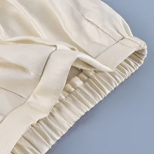 Close-up of elastic waistband on cream satin lantern trousers with smooth texture