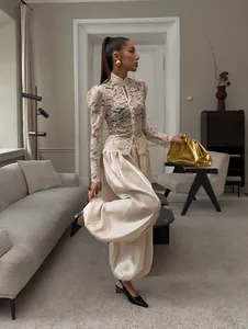Model wearing elegant cream satin lantern pants and a white lace blouse in an interior setting