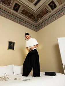 Asian model wearing black satin drape lantern pants in a stylish, artistic bedroom.