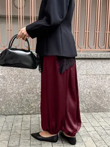 Dettaglio laterale di pantaloni harem in raso bordeaux con bordo in pizzo nero per donna