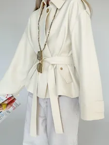 Close-up of elegant cream lapel windbreaker jacket with belted waist and pocket detail.