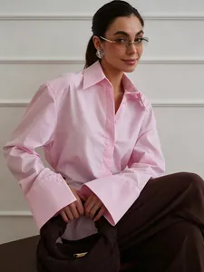 Détail d'un chemisier rose à manches longues avec poignets larges et col classique.