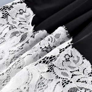 Close-up detail of delicate white floral lace trim on smooth black satin fabric.