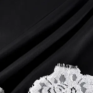 Close-up detail of elegant white lace embroidery on smooth black satin fabric texture