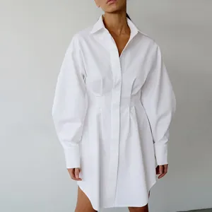 Detail van een witte overhemdjurk met lange mouwen, getailleerde taille en plooien
