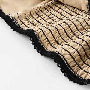 Detailed macro view of beige smocked fabric with black lace trim on a women's camisole