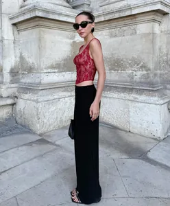 Fashionable model wearing a red lace camisole top and black pants against a stone wall.