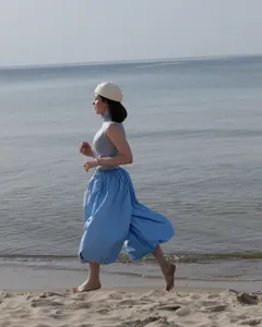 Stylish woman running on a sandy beach wearing light blue high-waisted balloon harem pants