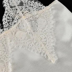Close-up detail of the delicate eyelash lace on a white satin V-neck camisole top.