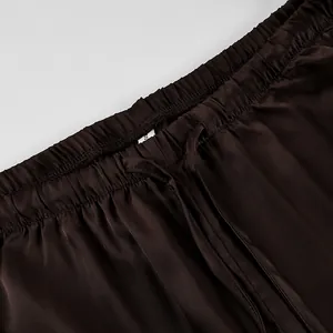 Detailed close-up of the elastic waistband and drawstring on brown satin trousers