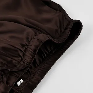 Close-up detail of the elastic waistband and smooth satin texture on these brown trousers.