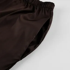 Detail shot of brown satin straight-leg trousers showing elastic waist and side pocket