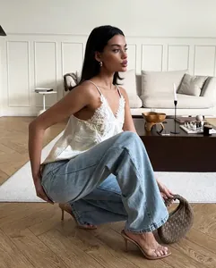 Elegant white satin cami top with delicate lace V-neck detail shown in a lifestyle pose