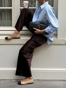 Detail of chocolate brown satin trousers with a smooth, draped finish.