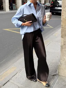 Detail of dark brown high-waist satin trousers with elegant drape in urban street setting.