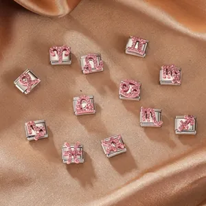 Dettaglio di ciondoli zodiacali con strass rosa su maglie modulari in acciaio