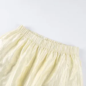 Close-up detail of the elastic waistband on loose shimmery pale yellow lantern pants