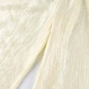 Close-up detail of champagne shiny pleated fabric for stylish loose-fit lantern pants