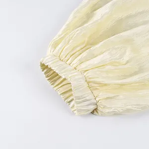 Close-up of elasticated cuff on cream pleated lantern pants showing fabric texture.